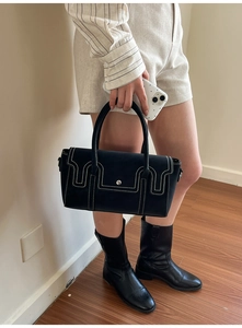 Détail d'un sac à main noir mat avec surpiqûres blanches et boucle ronde argentée