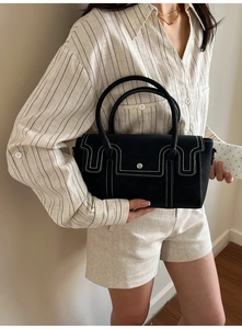 Close-up of black leather handbag with contrast stitching and metallic buckle detail