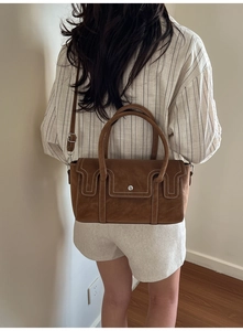Brown suede handbag with contrast stitching worn by model in a minimalist studio setting
