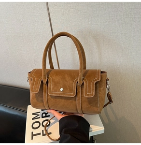 Detail of tan suede handbag with white contrast stitching and metallic buckle closure