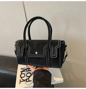 Detail of black cylindrical leather handbag featuring contrast white stitching and dual handles