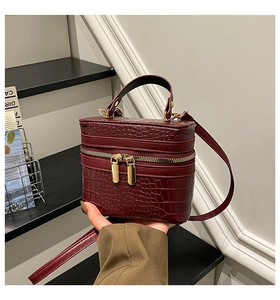 Detail of burgundy crocodile-embossed box bag with golden zippers and hand handle