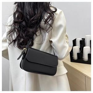 Gros plan du sac bandoulière noir en cuir avec boucle dorée porté par un mannequin