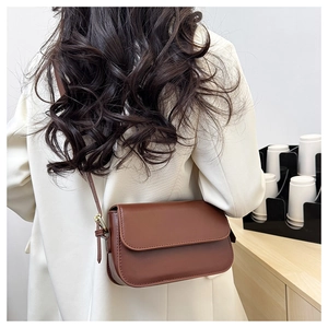 Sac bandoulière en cuir marron porté par un mannequin dans un intérieur minimaliste