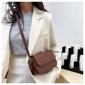 Gros plan d'un sac bandoulière en cuir marron porté avec un blazer blanc élégant