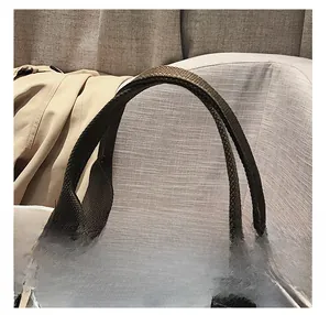 Close-up of brown woven handle with reinforced X-shaped stitching on white canvas tote bag