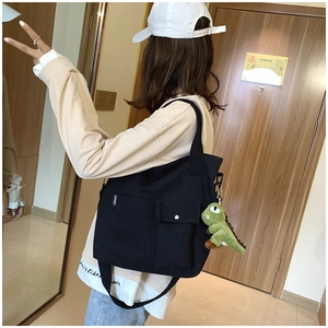Detail of black canvas tote bag with front pockets and cute green dinosaur plush charm