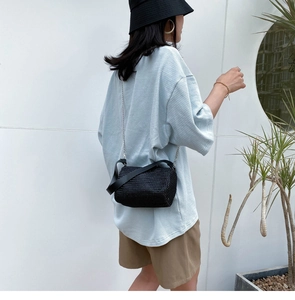 Détail d'un sac bandoulière cylindrique noir avec chaîne porté par un mannequin