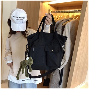 Detail of black canvas tote bag featuring external pockets and a green plush frog charm
