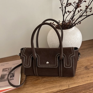 Retro dark brown leather handbag with contrast stitching and top handle on a wooden table
