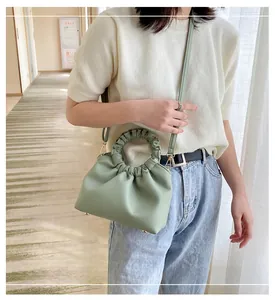 Detail of mint green ruched handbag with gold hardware and circular handle shown on model
