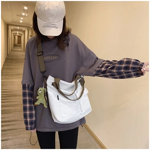 Detailed view of large white canvas tote bag with green straps and cute dragon charm