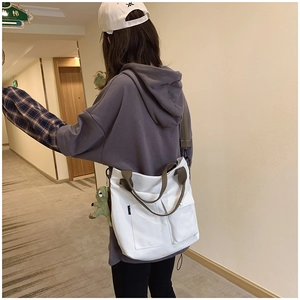 Detailed back view of a large white canvas tote bag with olive green straps and dinosaur charm