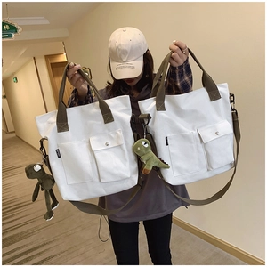 Canvas tote bag with green straps and decorative plush charms shown in a lifestyle setting