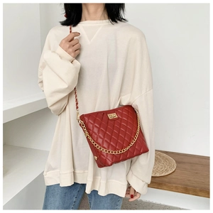Close-up of red quilted crossbody bag with gold chain strap and metal swivel lock on model