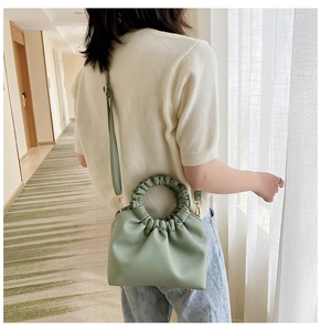 Detail view of a pale green ruched dumpling bag with a soft handle and leather strap