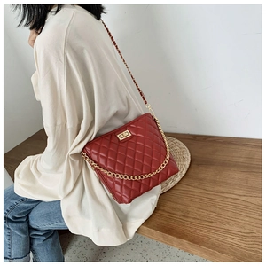 Detail of red quilted crossbody bag with gold chain strap and turn-lock closure