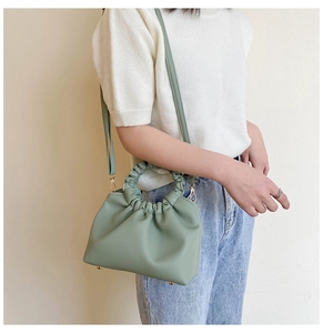 Model wearing a light green pleated cloud bag with a top handle and slim shoulder strap