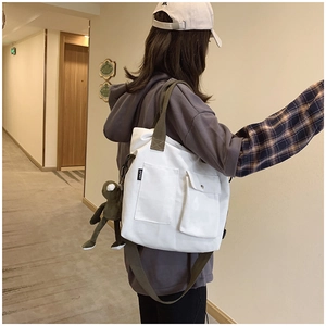 Detail of white canvas tote bag with olive green straps and a plush frog pendant
