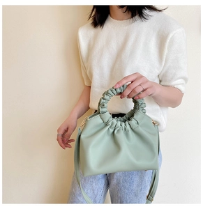 Detail of light green pleated handbag with circular handle and adjustable strap