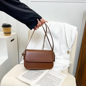Sac bandoulière minimaliste en cuir marron foncé sur un blazer blanc avec un café