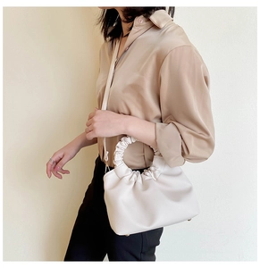 Close-up of white pleated cloud handbag with detachable strap held by a model