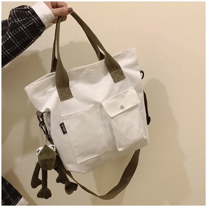 Close-up of white canvas tote bag with olive straps and green frog plush accessory