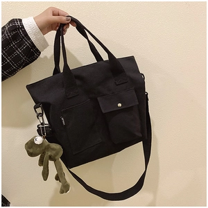 Detail of black canvas tote bag with dual front pockets and a cute frog plush pendant