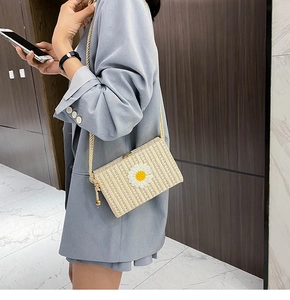 Détail d'un sac bandoulière en paille beige avec une marguerite 3D et une bandoulière en corde