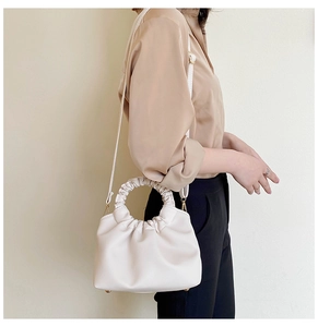 Detail of a creamy white pleated dumpling bag with matching round handle and gold hardware