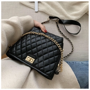 Detail of black quilted crossbody bag with golden chain strap and leather shoulder pad
