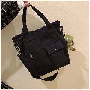 Detail of black canvas tote bag featuring external pockets and cute green dinosaur charm