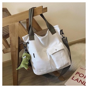 Close-up of a canvas tote bag on a chair featuring a green dinosaur plush keychain