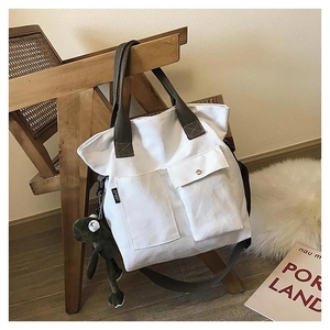 Close-up of a white canvas tote bag with green handles and a small dinosaur charm