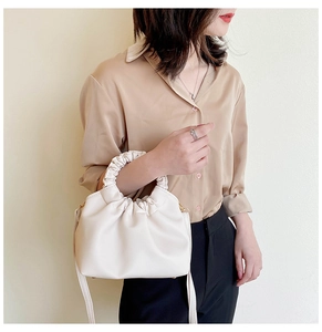 Detail of cream soft leather dumpling bag featuring a ruched handle and shoulder strap
