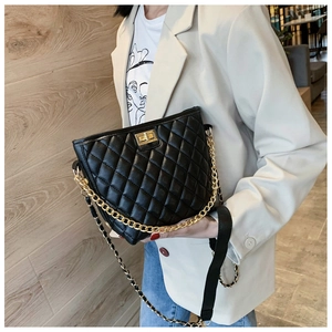 Detailed view of black quilted crossbody bag with gold chain strap on a female model