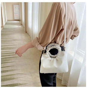 Detail of white pleated handbag featuring a round handle and gold hardware on model