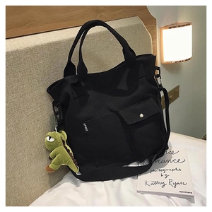 Detail of black canvas tote bag with Sport logo pocket and green dinosaur plush charm