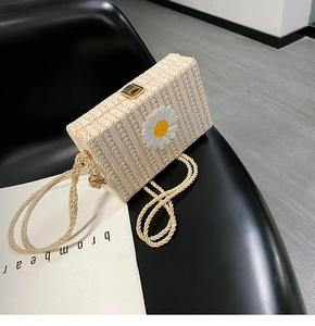 Détail d'un sac boîte en paille tissée beige avec applique marguerite et fermoir doré