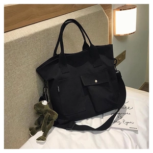 Detail of black canvas tote bag with front pockets and cute green frog plush keychain