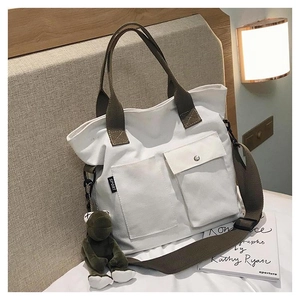 Detail of white canvas tote with brown straps, sport label, and cute green frog pendant