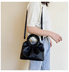 Detail of black crossbody bag with pleated round handle and golden metal studs