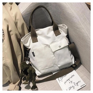 Detail of canvas tote bag with front pockets and green frog charm on a gray sofa