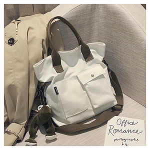 Detail of white canvas tote with green straps, dual front pockets, and plush frog charm