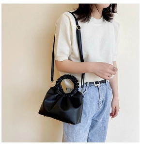 Chic black matte PU leather handbag with ruched handles and gold metal studs on white attire