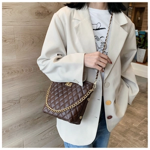Brown quilted crossbody bag with gold chain strap worn by model in beige suit