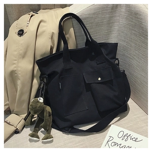 Detail of black canvas tote bag featuring dual front pockets and a cute frog charm
