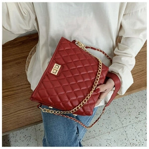 Close-up of red quilted crossbody bag with gold chain strap on a model's lap