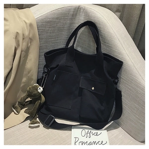 Detail of black canvas tote bag featuring front utility pockets and a green frog keychain