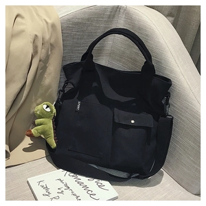 Detail of black canvas tote bag with front pockets, SPORT label, and green dinosaur charm